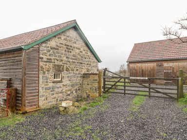 A gravel driveway with a wooden gate and two buildings with stone and wooden walls at Old Cary Cottage Henley near Langport