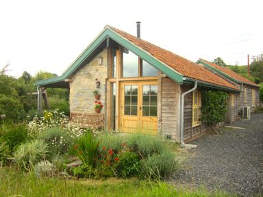 A cottage with a tiled roof wooden doors and windows a garden with flowers and shrubs and a gravel path at Old Cary Cottage Henley near Langport