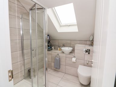 A bathroom with a glass shower enclosure a wall-mounted toilet a round sink under a skylight at St Julien in Dawlish