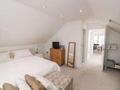 A bedroom with a large bed pillows a wooden dresser with a tv a mirror an ottoman and an open door showing an adjacent room at St Julien in Dawlish