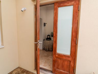 An open wooden door with frosted glass panel leading to a room with a round table covered with a checkered cloth a clock and flowers at St Julien in Dawlish