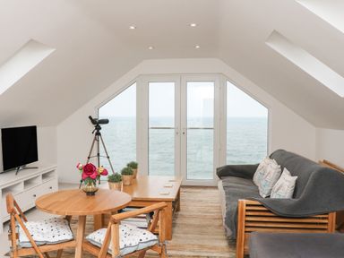 A living room with wooden furniture and a telescope by large windows overlooking the sea at St Julien in Dawlish