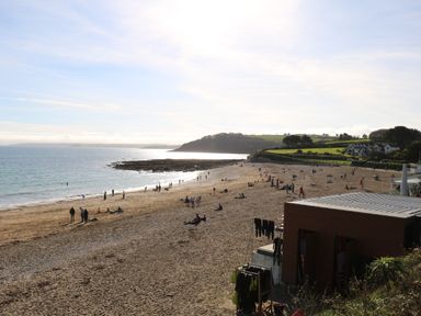 A sandy beach with people near the water and a small building with wetsuits hanging at Chycoose Hicks Mill near Perranarworthal