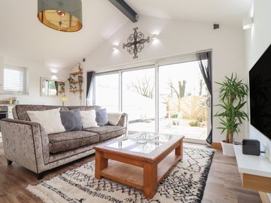 A living room with a sofa, coffee table, potted plant, wall-mounted TV, and glass sliding doors at Chycoose Hicks Mill near Perranarworthal