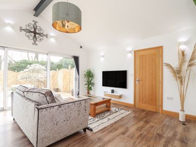 A living room with a sofa coffee table wall mounted tv and sliding glass doors at Chycoose in Hicks Mill near Perranarworthal