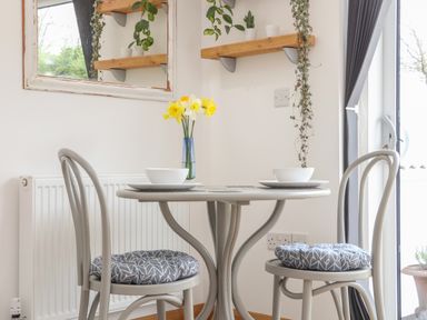 A dining table with two chairs and bowls with flowers in a vase on the table at Chycoose Hicks Mill near Perranarworthal