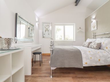 A bedroom with a metal bed frame a floral bedspread a white desk a black stool and wooden floor at Chycoose Hicks Mill near Perranarworthal