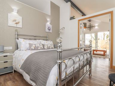 A bedroom with a metal frame bed and floral bedding looking into a living room at Chycoose in Hicks Mill near Perranarworthal