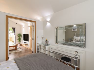 A bedroom with a metal bed frame a dressing table and a mirror looking into a living room with a TV and a plant at Chycoose in Hicks Mill near Perranarworthal