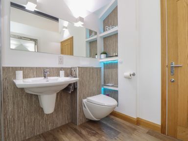 A bathroom with a wall-mounted sink and toilet wooden cabinets and shelves with decorative items at Chycoose Hicks Mill near Perranarworthal