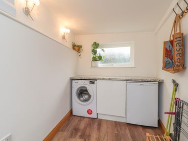 A utility room with a washing machine fridge countertop window and bags hanging on hooks at Chycoose Hicks Mill near Perranarworthal