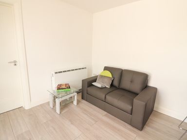 A small living room with a grey sofa and a glass side table with books at Coolnaharragill Lower Annexe in Glenbeigh County Kerry