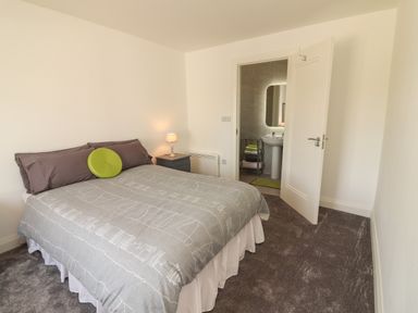 A bedroom with a bed a nightstand with a lamp and an open door leading to a bathroom at Coolnaharragill Lower Annexe in Glenbeigh County Kerry
