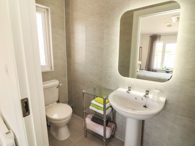 A bathroom with a toilet sink mirror and glass shelf with towels at Coolnaharragill Lower Annexe in Glenbeigh County Kerry