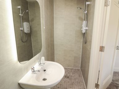 A bathroom with a sink a mirror a shower head and a tiled floor at Coolnaharragill Lower Annexe in Glenbeigh County Kerry