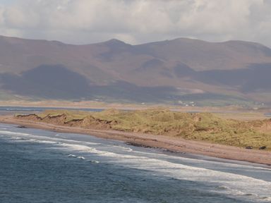 A coastal beach with sand dunes and ocean waves against mountain backdrop at Coolnaharragill Lower Annexe in Glenbeigh County Kerry