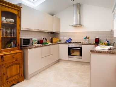 A kitchen with beige cabinets a wooden cupboard a microwave an oven a gas stove and kitchen utensils at Fern Cottage in Ambleside