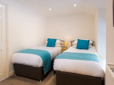 A bedroom with two single beds with blue cushions and throws and a bedside table with a lamp at Fern Cottage in Ambleside
