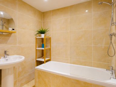 A bathroom with a bathtub a showerhead a sink a round mirror and a corner shelf with a plant at Fern Cottage in Ambleside