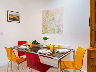 A dining room with a glass table set for four with plates glasses of orange juice a bowl of salad and a vase of white flowers at Fern Cottage in Ambleside