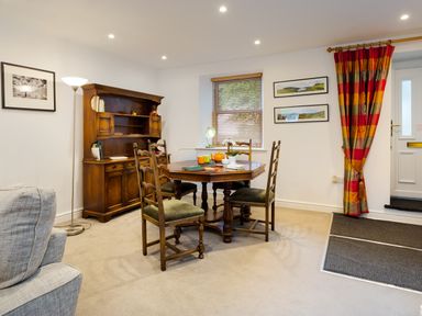 A dining area with a wooden table and chairs a wooden cabinet a floor lamp and red striped curtains at Fern Cottage in Ambleside