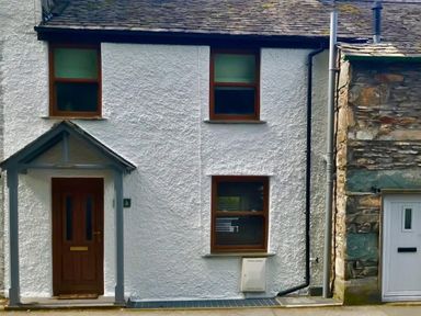A white house with two windows and a wooden door next to a stone building at Fern Cottage in Ambleside