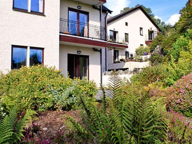 The exterior of a two story house with balconies and a garden with various plants and bushes at Romney 12 in Waterhead near Ambleside