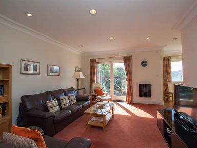 A living room with leather sofas coffee table TV and glass doors leading to a garden at Romney 12 Waterhead near Ambleside