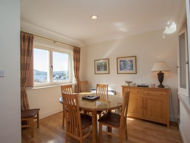 A dining room with a round table and wooden chairs next to a window at Romney 12 Waterhead near Ambleside