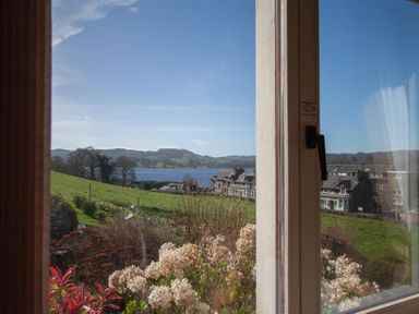A window view of a garden with flowers a grassy hill houses and a lake with hills in the background at Romney 12 Waterhead near Ambleside