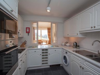 A kitchen with white cabinets a washing machine a sink a kettle and a view into a dining area at Romney 12 Waterhead near Ambleside