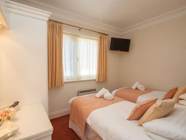A bedroom with two single beds a window with curtains and a wall-mounted television at Romney 12 Waterhead near Ambleside