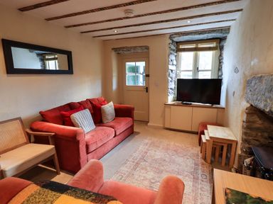 A living room with two red sofas a wooden chair a television on a cabinet a wooden door and a window with stone framing at Penny Red Cottage in Ambleside