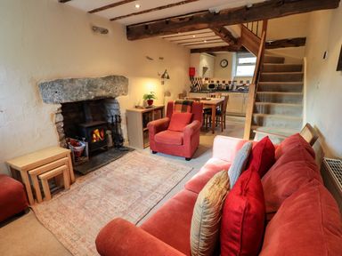 A living room with a fireplace armchairs a sofa stairs and a dining area at Penny Red Cottage in Ambleside