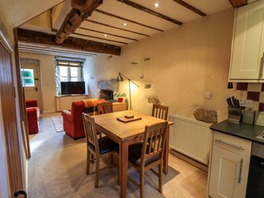 A dining area with wooden table and chairs next to a small kitchen and living area at Penny Red Cottage in Ambleside