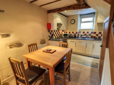 A kitchen with a wooden dining table and four chairs white cabinets and appliances at Penny Red Cottage in Ambleside