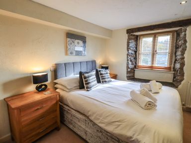 A bedroom with a double bed two bedside tables with lamps and a window with stone trim at Penny Red Cottage Ambleside