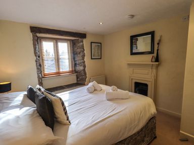 A bedroom with a bed pillows rolled towels window with blinds and a decorative fireplace at Penny Red Cottage in Ambleside