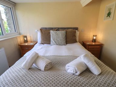 A bedroom with a bed with rolled towels on it two bedside tables with lamps and a window at Penny Red Cottage in Ambleside