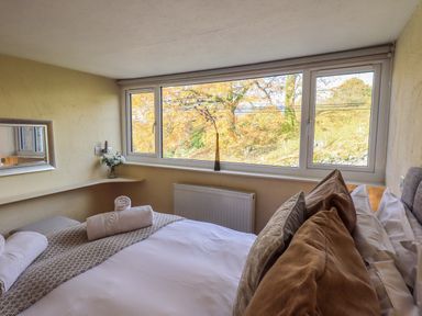A bedroom with a bed pillows and towels near a window with a view of trees at Penny Red Cottage in Ambleside