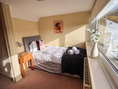 A bedroom with a single bed a bedside table with a lamp and a vase with flowers on the window ledge at Penny Red Cottage in Ambleside