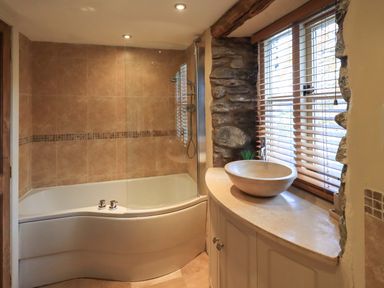 A bathroom with a bathtub shower combination and a round sink on a countertop by a window with blinds at Penny Red Cottage in Ambleside