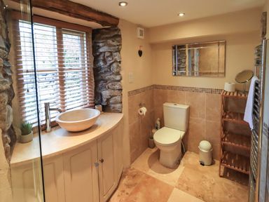 A bathroom with a toilet wooden shelving unit and a sink under a window with blinds at Penny Red Cottage in Ambleside