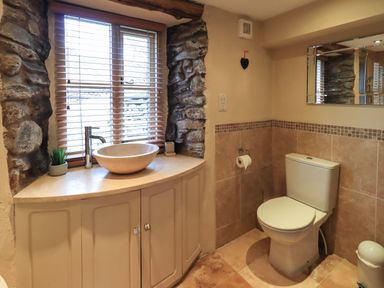 A bathroom with a stone framed window sink countertop toilet and wall mirror at Penny Red Cottage in Ambleside