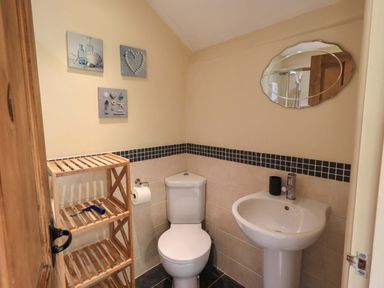 A bathroom with a toilet sink wooden shelving and wall decorations at Penny Red Cottage in Ambleside