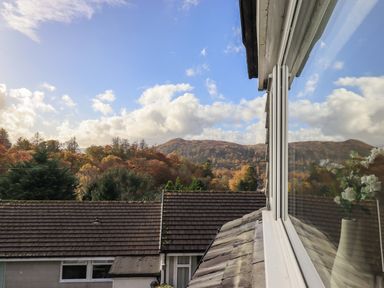 View of rooftops trees and hills with a window reflecting flowers at Penny Red Cottage in Ambleside
