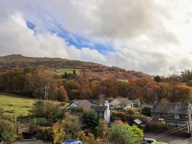 A rural village with houses surrounded by trees and hills under a cloudy sky at Penny Red Cottage in Ambleside