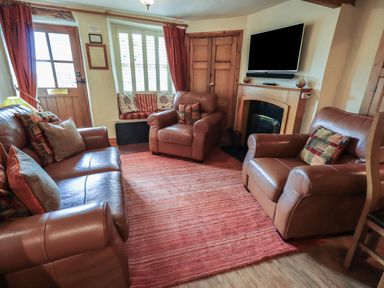 A living room with leather sofas a red rug a window seat and a wall mounted television at Heron Cottage in Ambleside