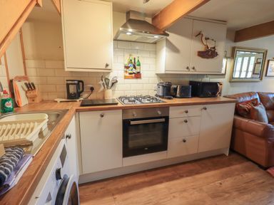 A kitchen with white cabinets wooden countertops a gas stove oven sink and various appliances at Heron Cottage in Ambleside