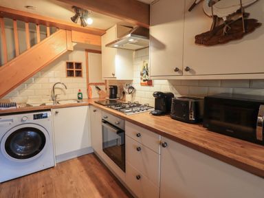 A kitchen with wooden countertops a washing machine a stove a microwave a toaster and under stairs storage at Heron Cottage in Ambleside